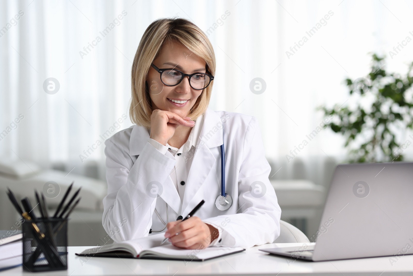 Photo of Smiling doctor with laptop having online consultation at table in office