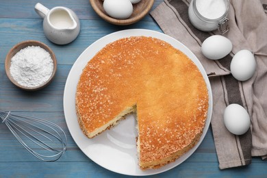 Photo of Tasty sponge cake, whisk and ingredients on light blue wooden table, flat lay