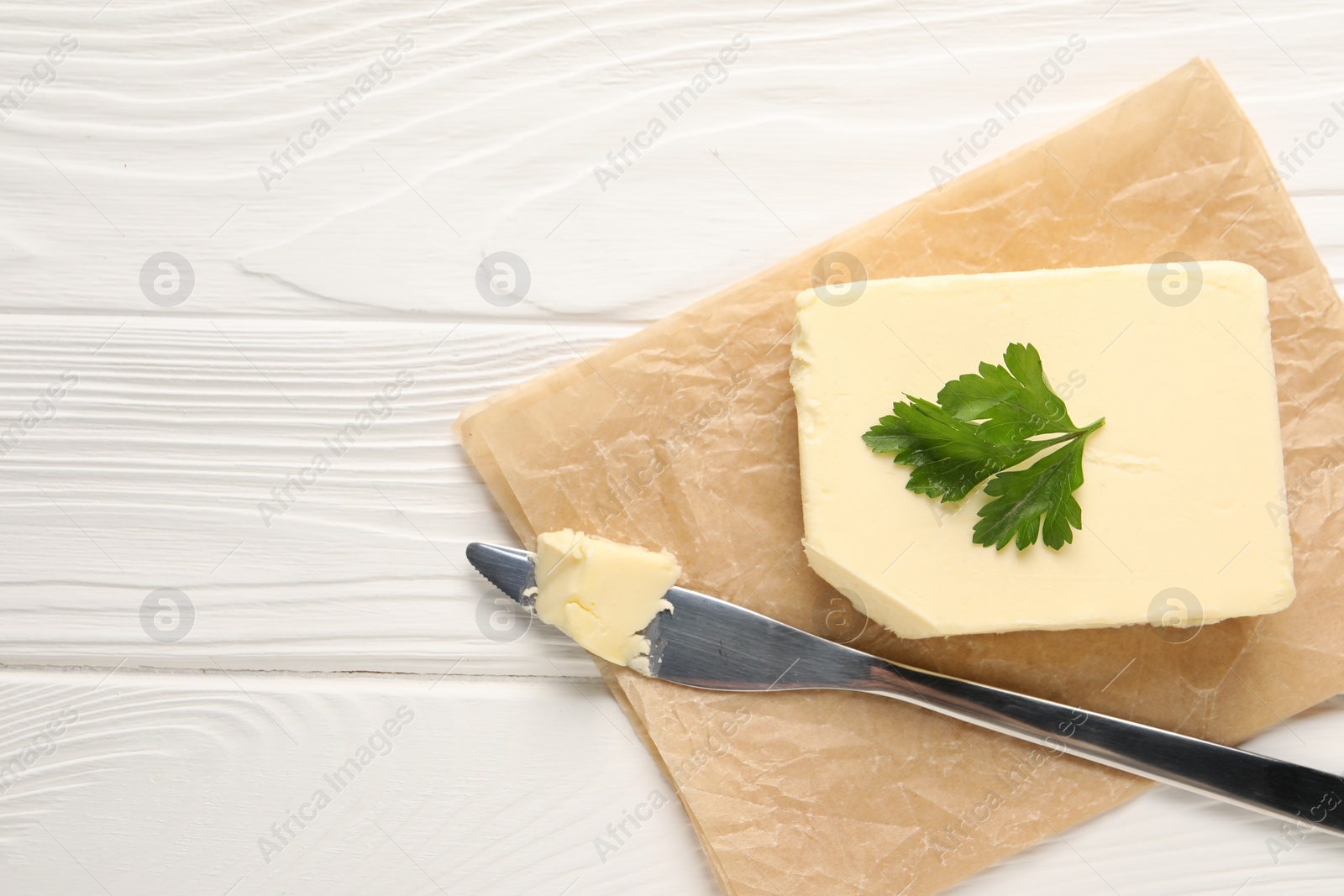 Photo of Tasty butter and knife on white wooden table, top view. Space for text