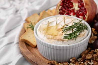 Photo of Board with tasty baked camembert and rosemary in bowl on table, closeup. Space for text