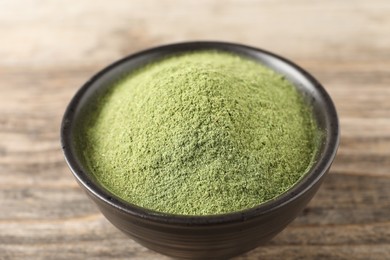 Wheat grass powder in bowl on wooden table, closeup