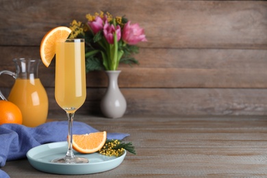 Glass of Mimosa cocktail with garnish on wooden table. Space for text