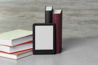 Photo of Portable e-book reader and many hardcover books on white textured table, space for text