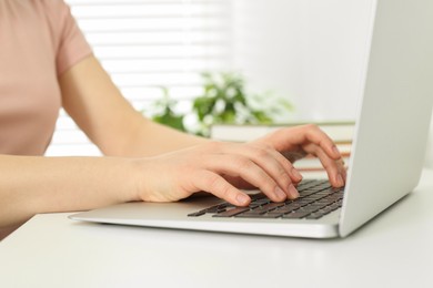 Home workplace. Woman typing on laptop at white desk indoors, closeup