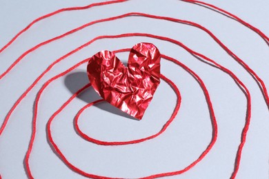 Red crumpled paper heart and thread on gray background, closeup