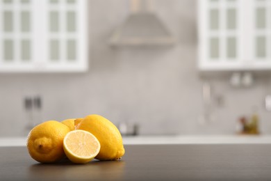Whole and cut lemons on wooden counter in kitchen, space for text