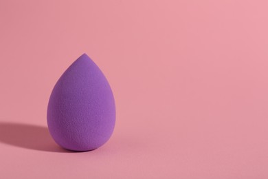 Photo of Purple makeup sponge on pink background. Space for text