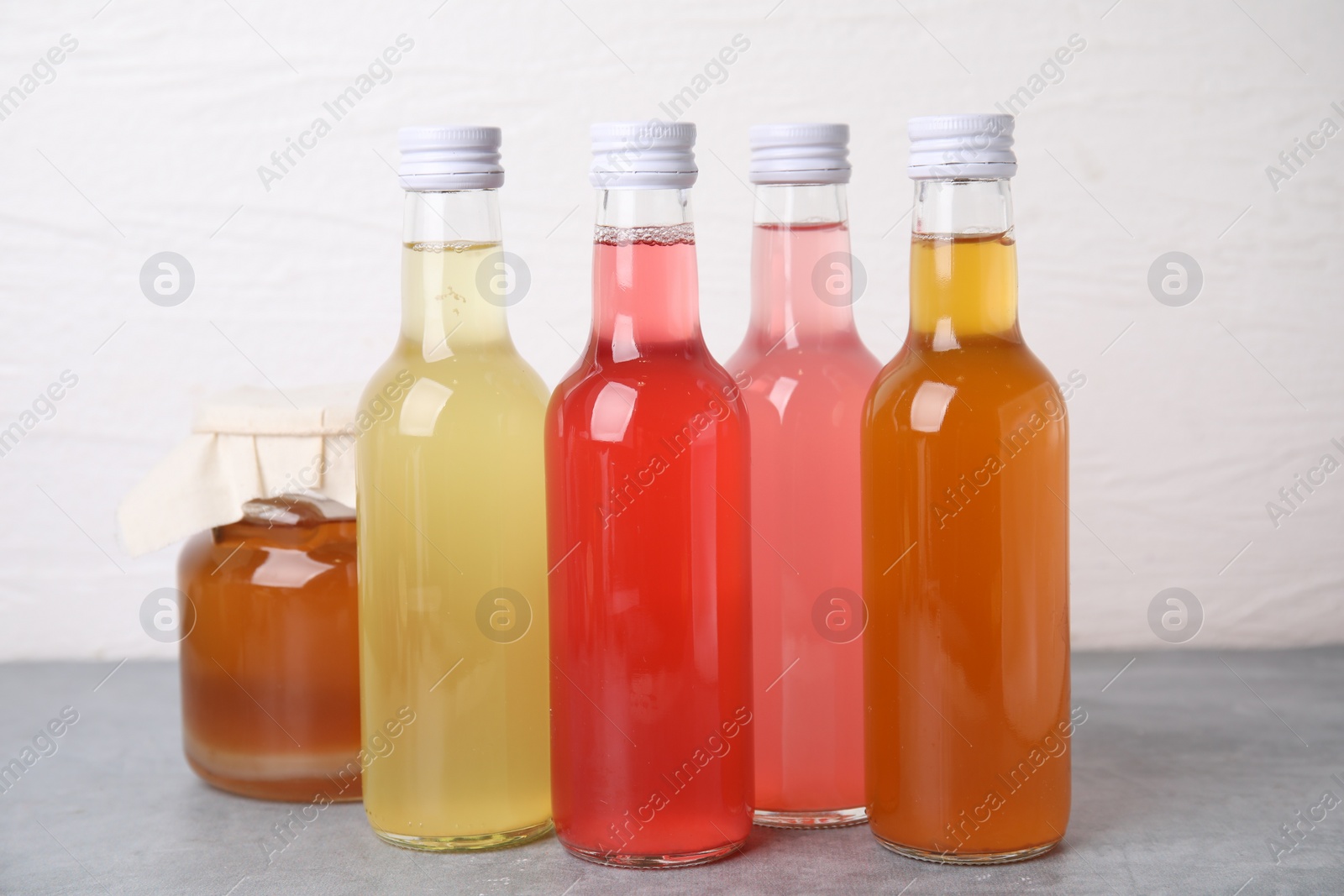 Photo of Delicious kombucha in glass bottles and jar on grey table against white background