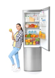 Young woman with apple near open refrigerator on white background