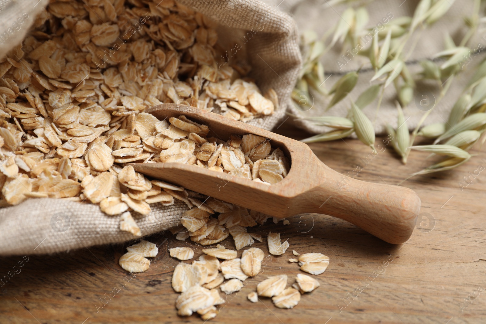 Photo of Bag with oatmeal, floret branches and scoop on wooden table, closeup