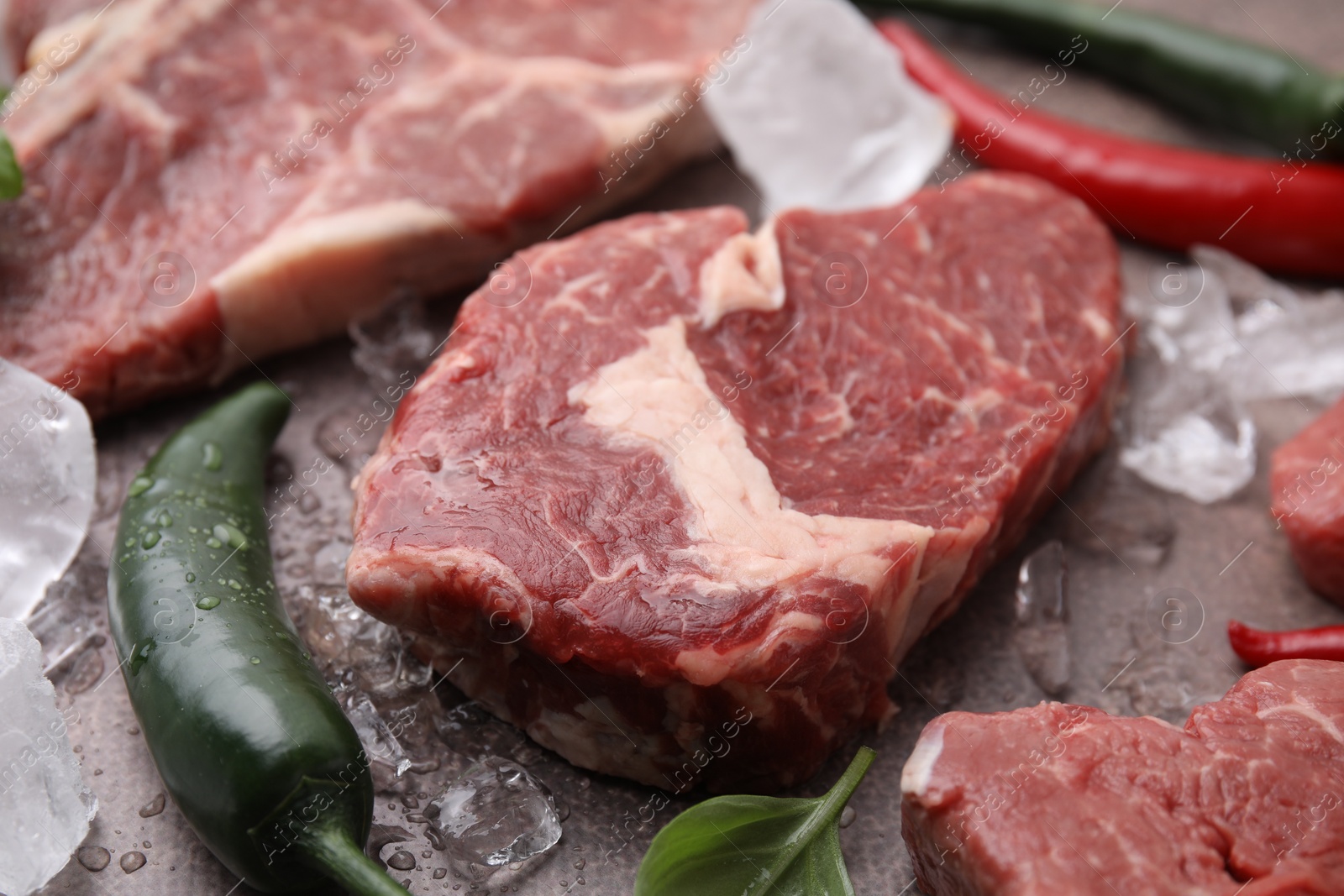 Photo of Fresh raw cut beef, ice cubes and spices on brown table, closeup