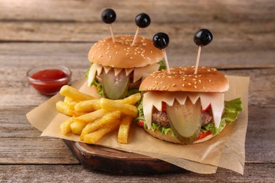Photo of Cute monster burgers served with french fries and ketchup on wooden table. Halloween party food