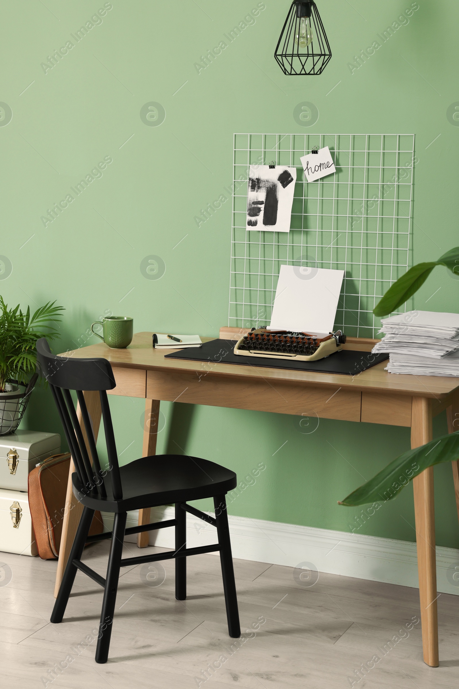 Photo of Typewriter, stack of papers and mood board on wooden table near pale green wall. Writer's workplace