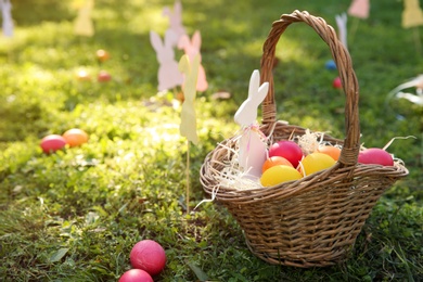 Basket with Easter eggs and decor on grass in park. Space for text