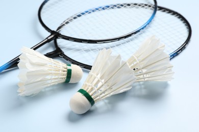 Photo of Feather badminton shuttlecocks and rackets on light blue background, closeup