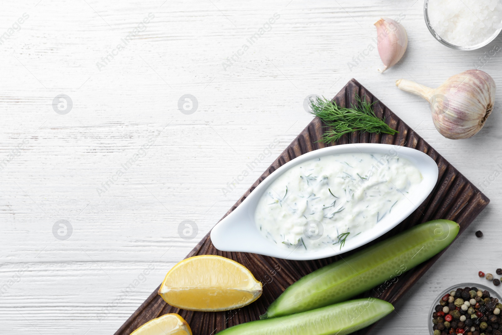 Photo of Tzatziki sauce with lemon, cucumber, dill and pepper on white wooden background, top view. Space for text