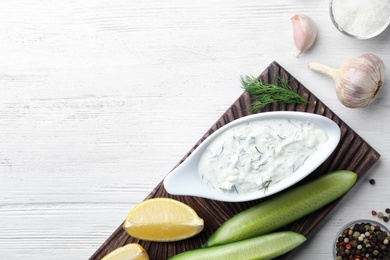 Photo of Tzatziki sauce with lemon, cucumber, dill and pepper on white wooden background, top view. Space for text