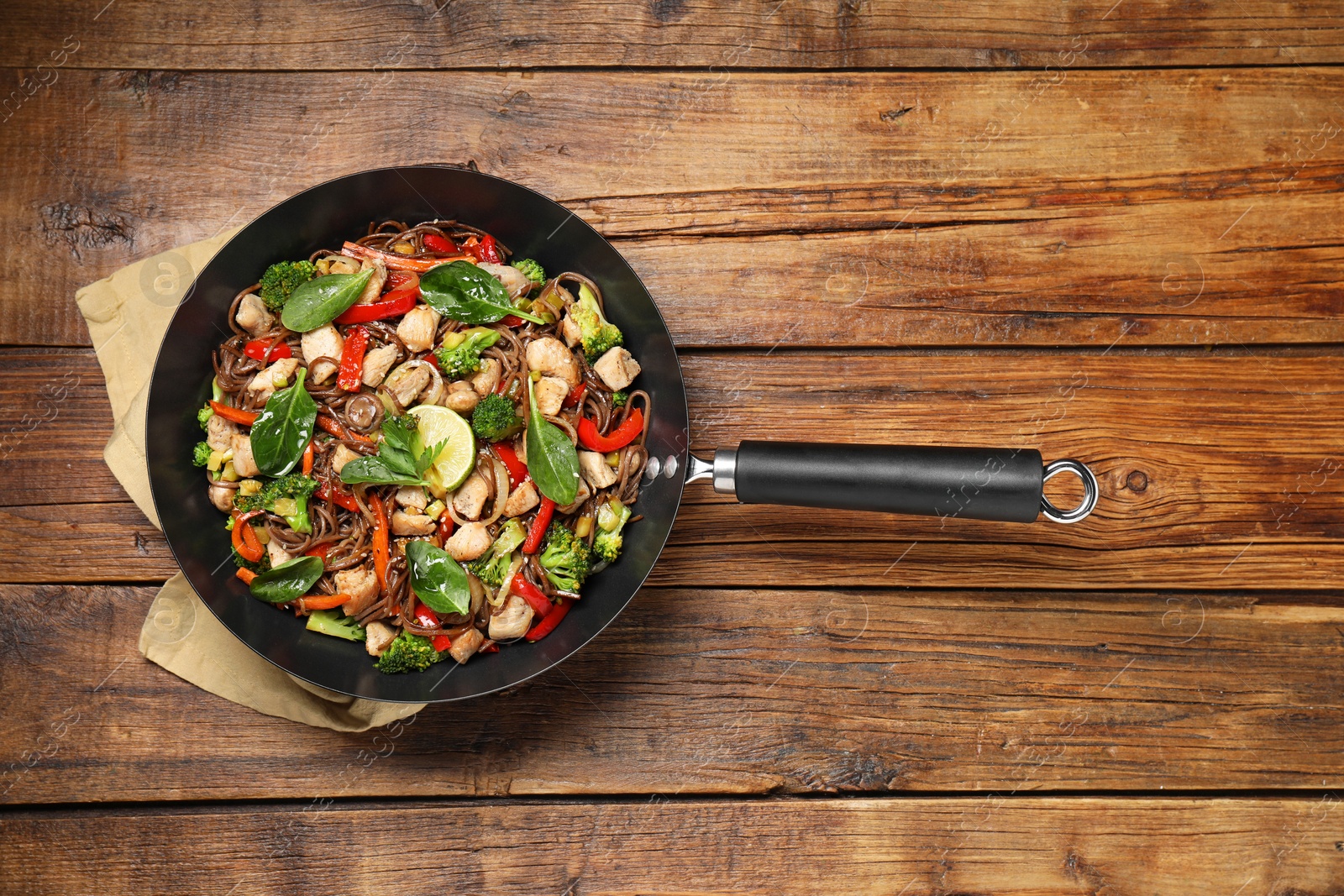 Photo of Stir-fry. Tasty noodles with meat and vegetables in wok on wooden table, top view