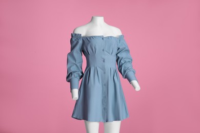 Female mannequin dressed in stylish light blue dress with necklace on pink background