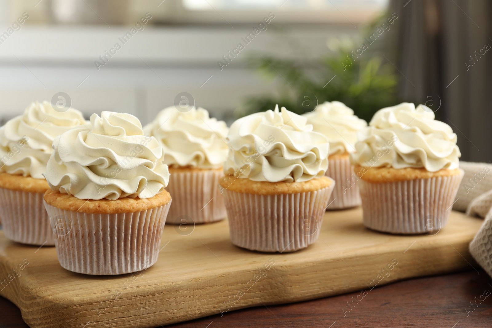 Photo of Tasty cupcakes with vanilla cream on wooden table, closeup