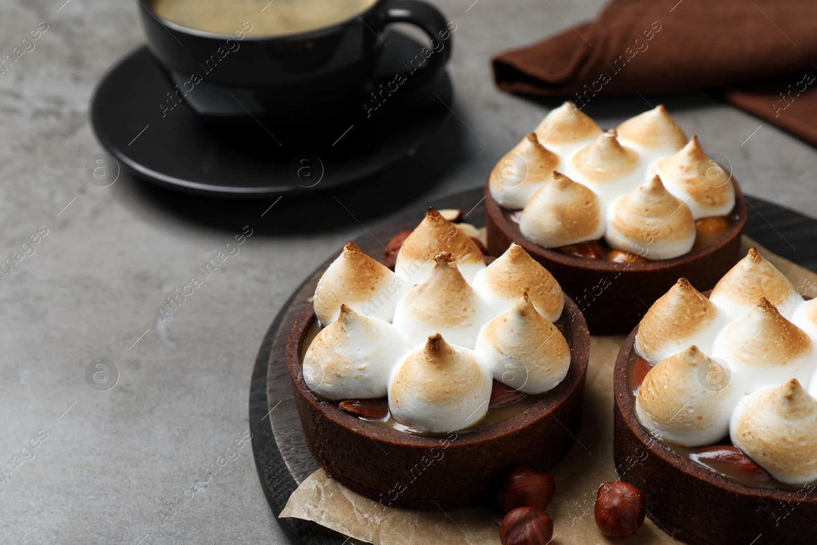 Photo of Delicious salted caramel chocolate tarts with meringue and hazelnuts on grey table, closeup