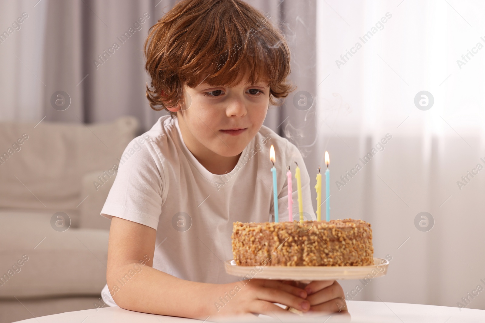 Photo of Cute boy with birthday cake at table indoors