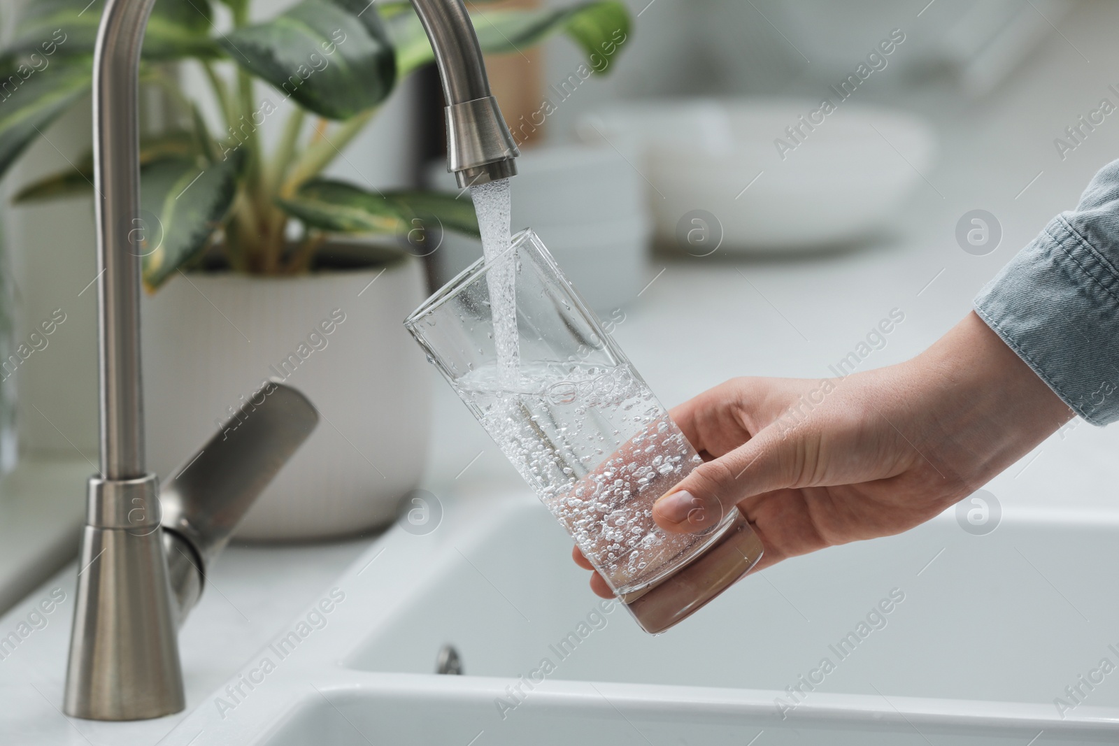 Photo of Woman filling glass with water from tap in kitchen, closeup