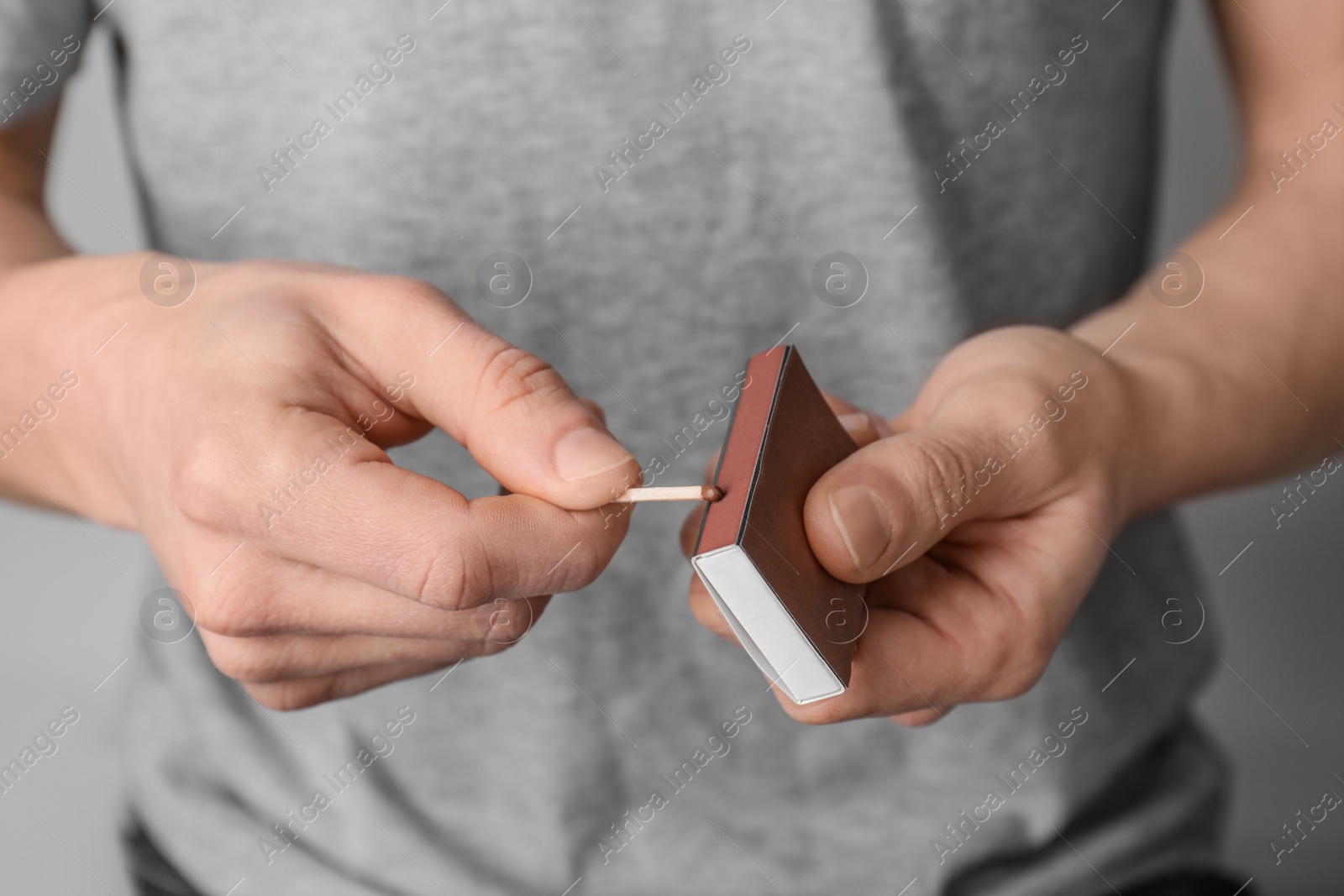 Photo of Man with box of matches on grey background, closeup