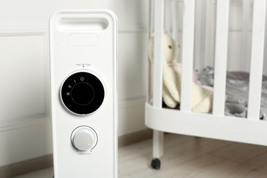 Photo of Modern portable electric heater and baby crib indoors, closeup. Space for text