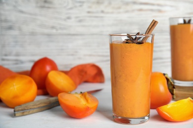 Photo of Tasty persimmon smoothie with anise and cinnamon on white wooden table. Space for text