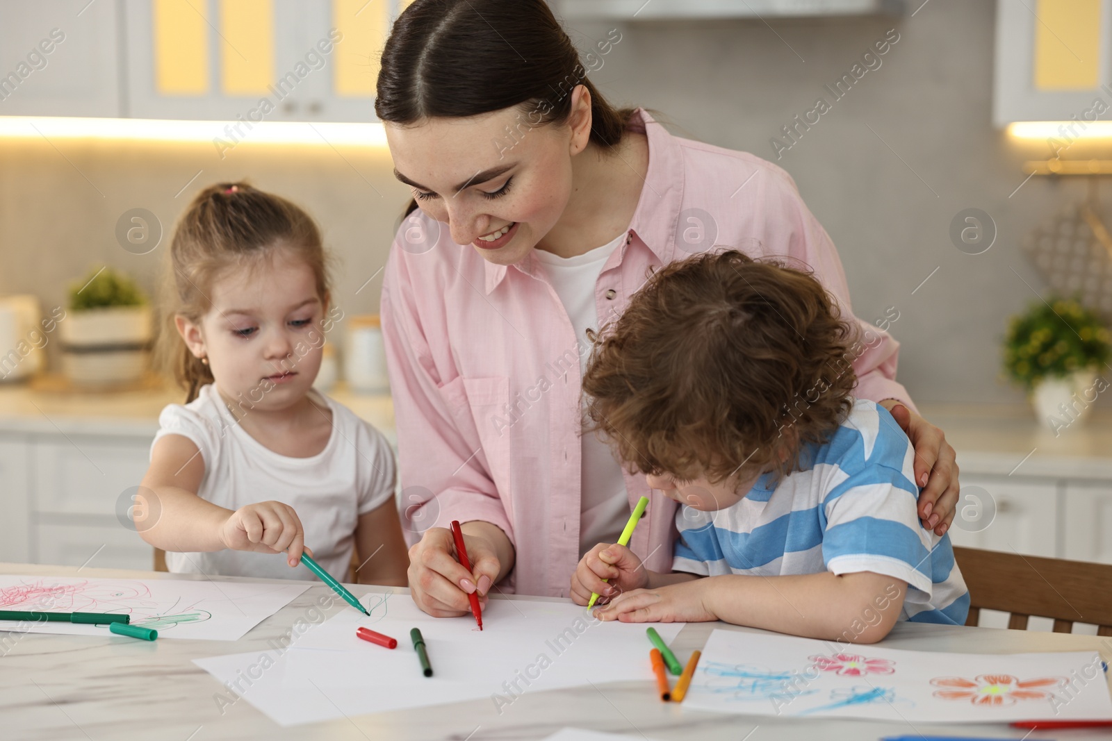 Photo of Mother and her little children drawing with colorful markers at table in kitchen