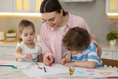 Photo of Mother and her little children drawing with colorful markers at table in kitchen