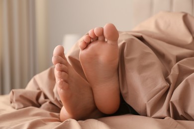 Photo of Person in bed with brown linens at home, closeup on feet