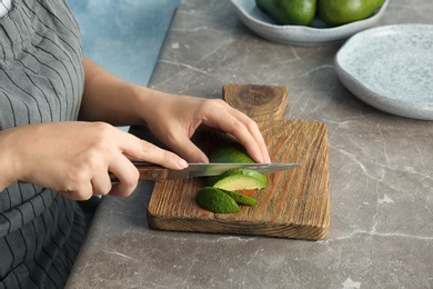 Photo of Woman cutting ripe avocado on wooden board at table