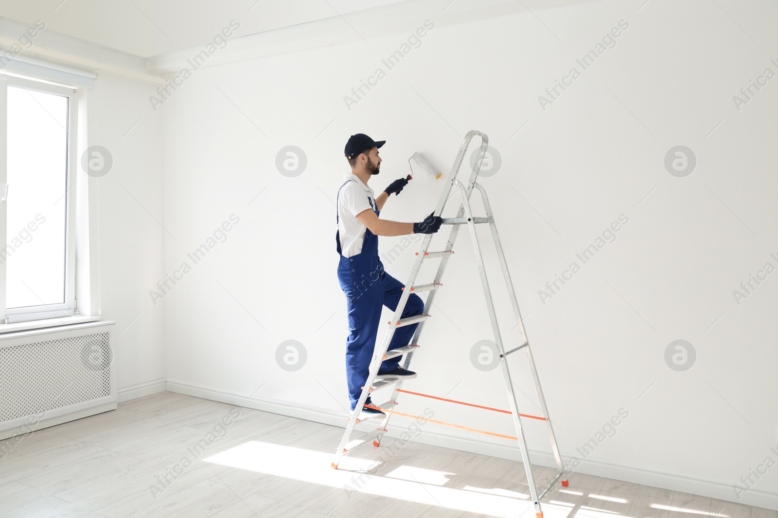 Photo of Handyman painting wall with roller brush indoors. Professional construction tools