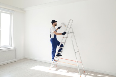 Photo of Handyman painting wall with roller brush indoors. Professional construction tools