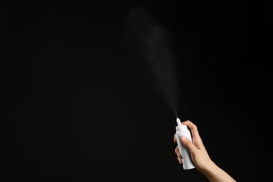 Photo of Nasal congestion. Woman spraying remedy from bottle on black background, closeup with space for text