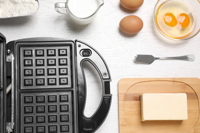 Flat lay composition with ingredients and Belgian waffle maker on white wooden table