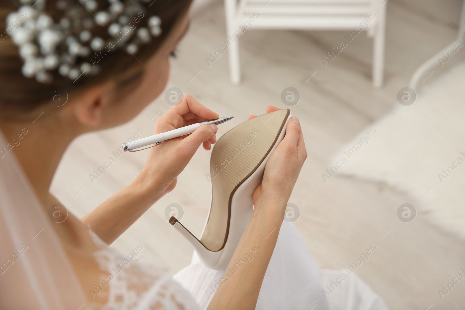 Photo of Young bride writing on her shoe indoors, closeup. Wedding superstition