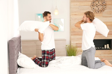 Happy gay couple having pillow fight on bed at home