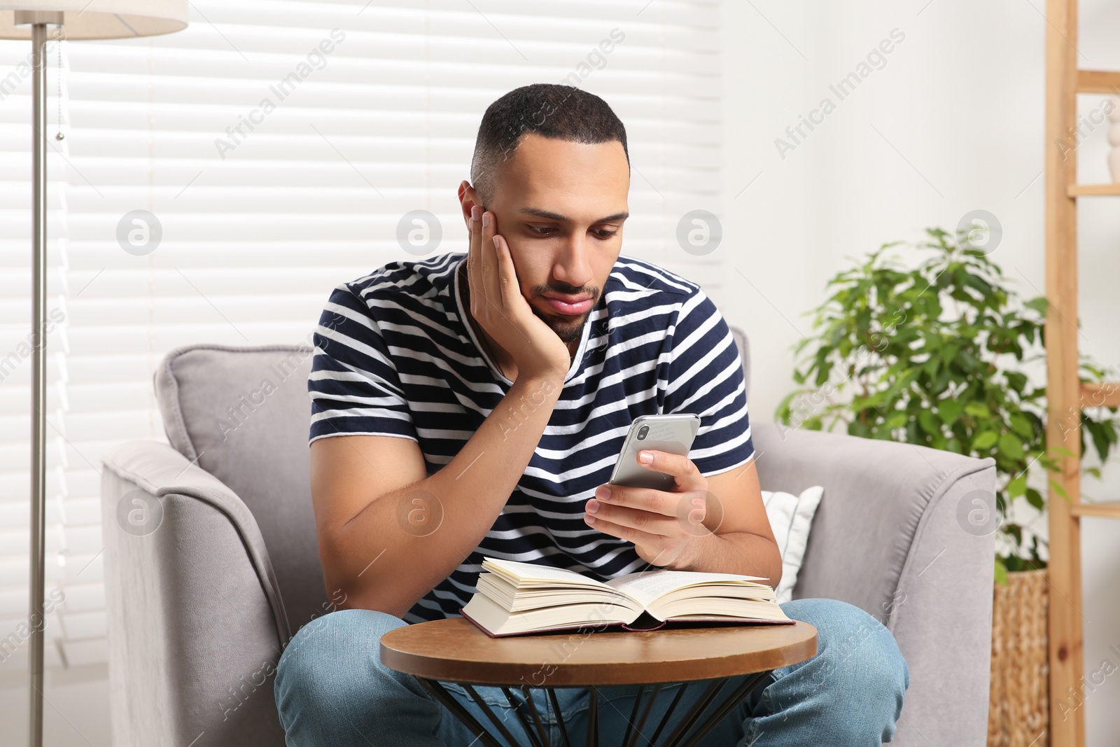 Photo of Young man using smartphone while reading book at home. Internet addiction