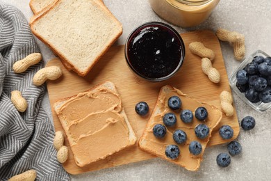 Photo of Tasty peanut butter sandwiches with fresh blueberries jam and peanuts on gray table, flat lay