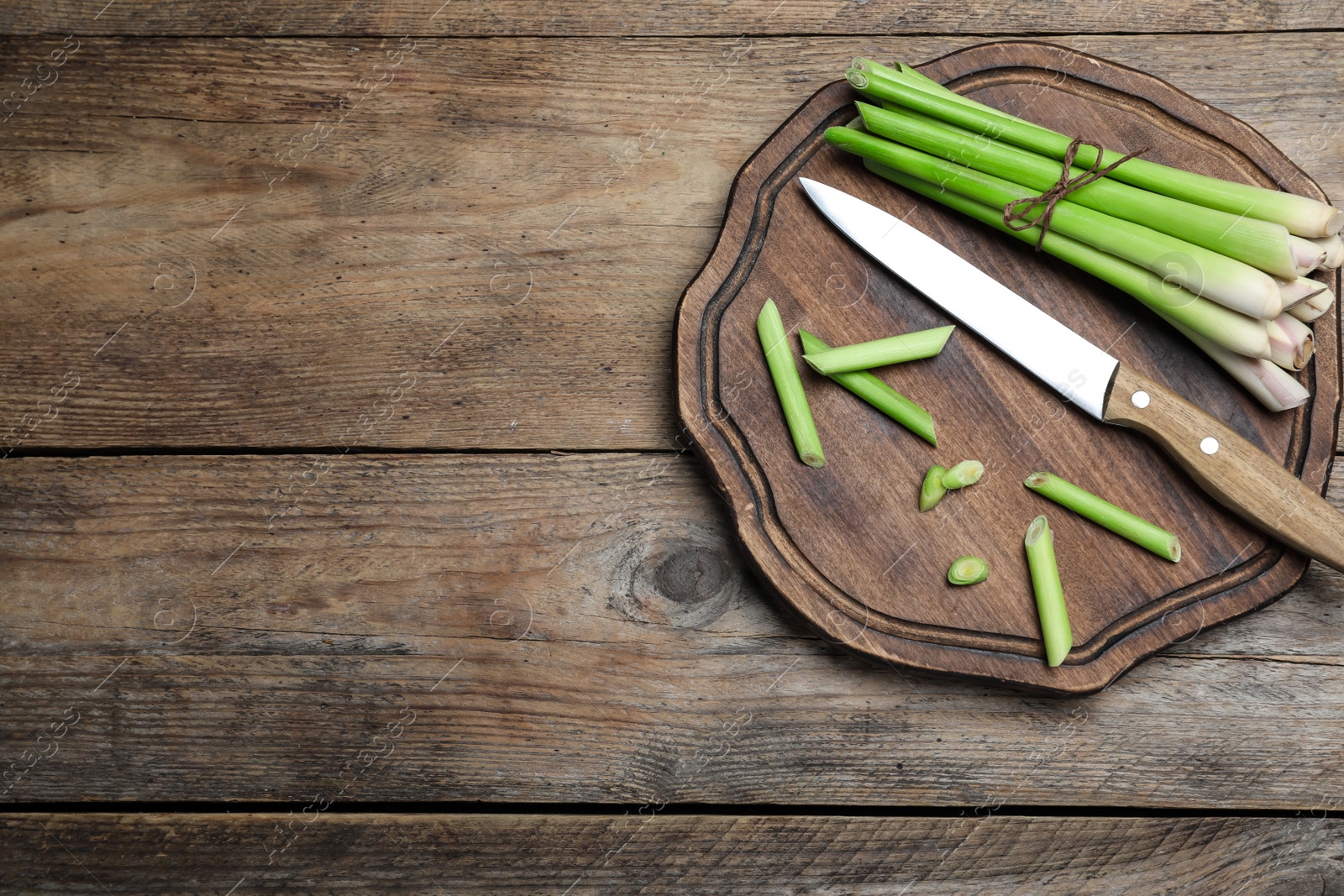 Photo of Fresh lemongrass, knife and cutting board on wooden table, top view. Space for text