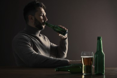 Photo of Addicted man drinking alcohol at wooden table indoors, focus on glass of beer
