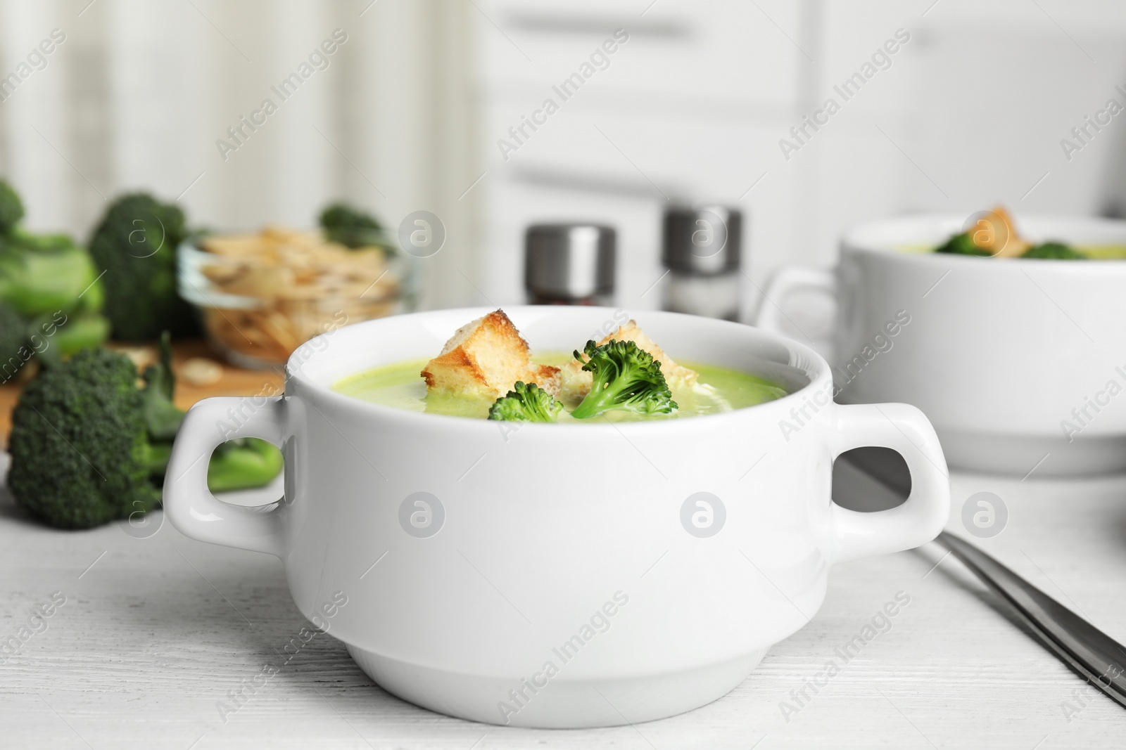 Photo of Delicious broccoli cream soup with croutons served on white wooden table indoors