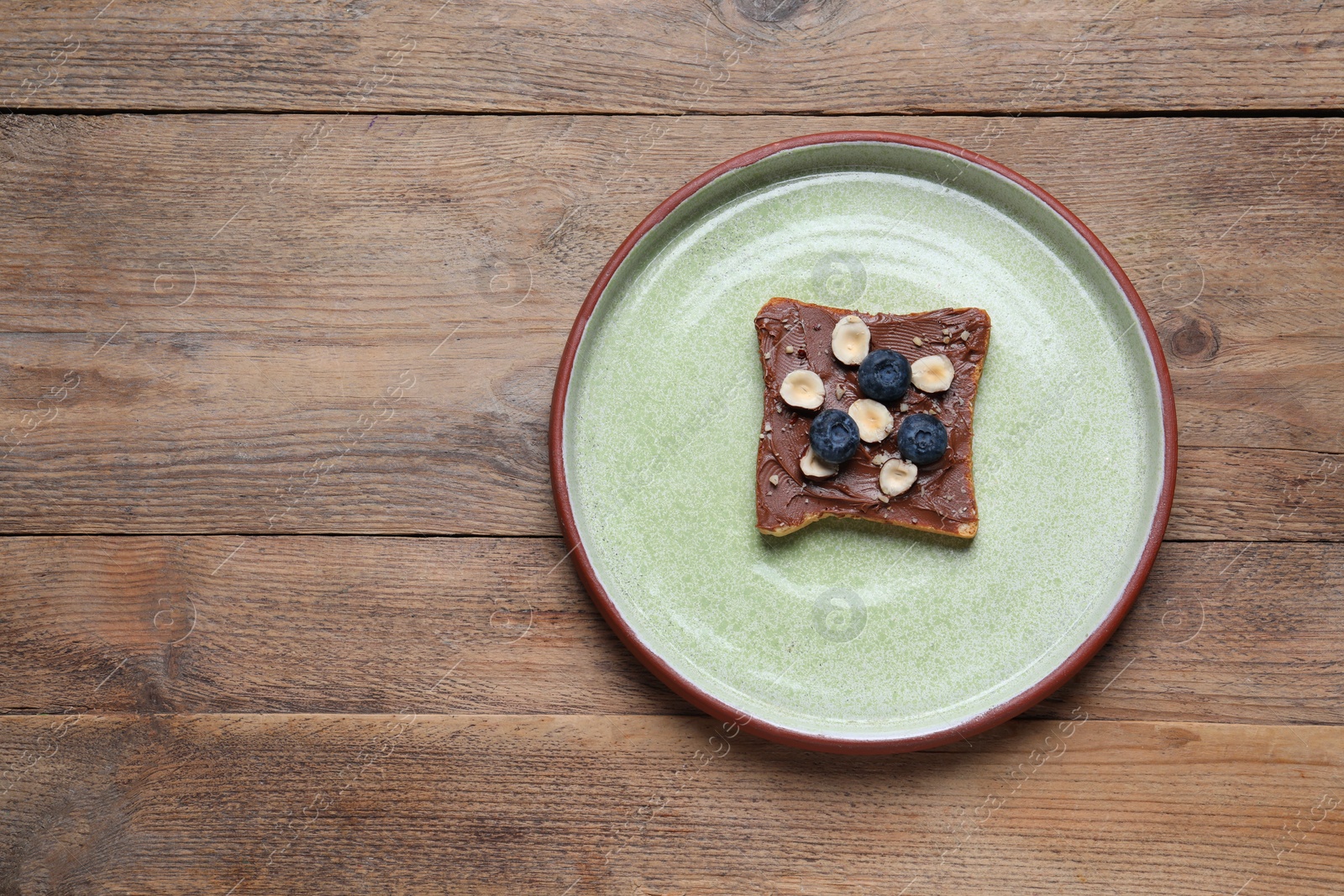 Photo of Toast with tasty nut butter, jam, blueberries and nuts on wooden table, top view. Space for text