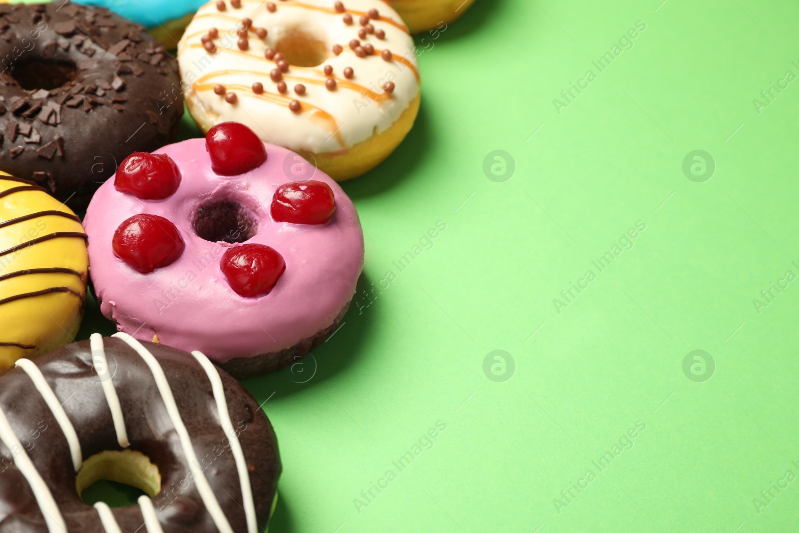 Photo of Sweet tasty glazed donuts on green background, closeup. Space for text