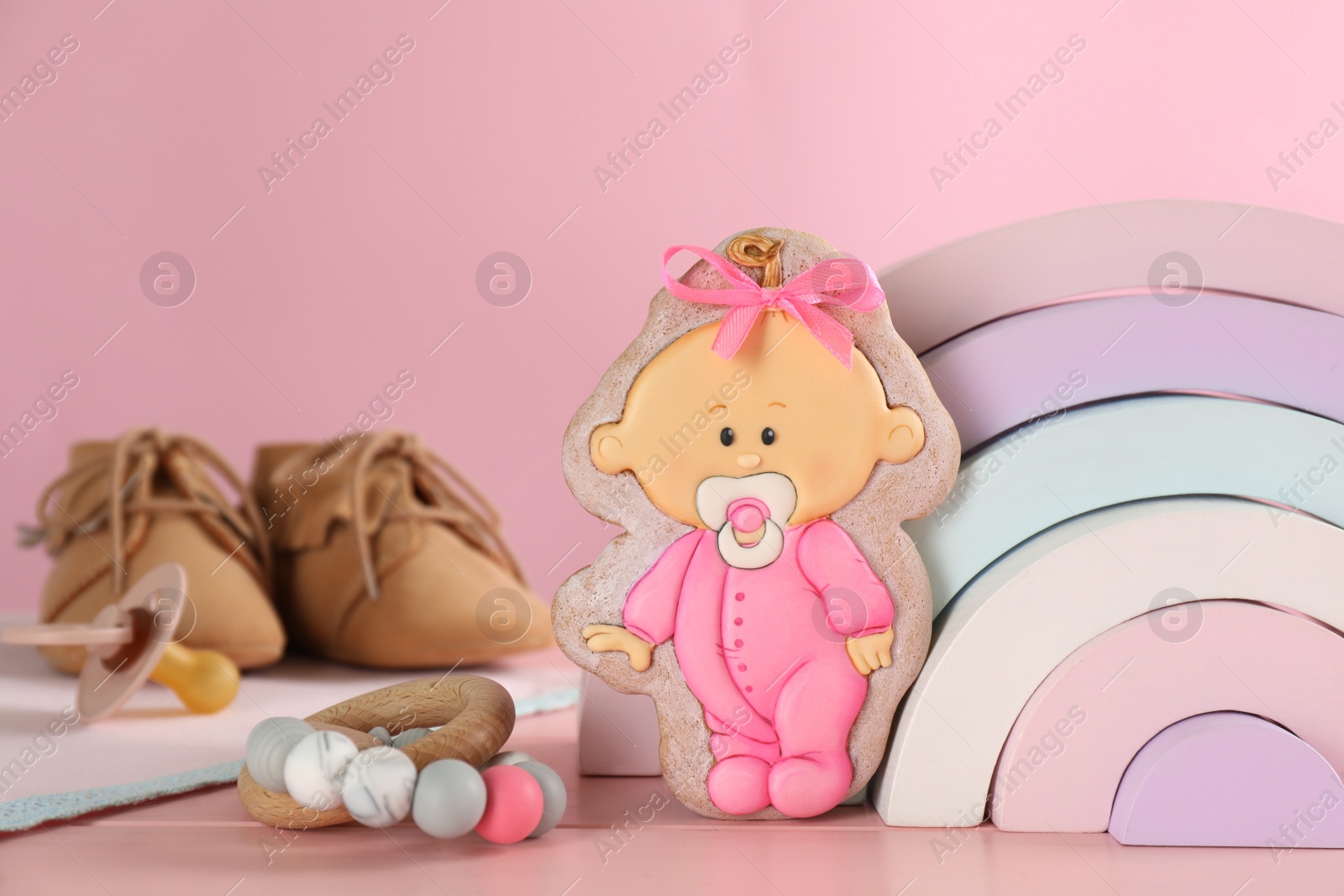 Photo of Tasty cookie in shape of cute baby, toys and booties on pink wooden table. Space for text