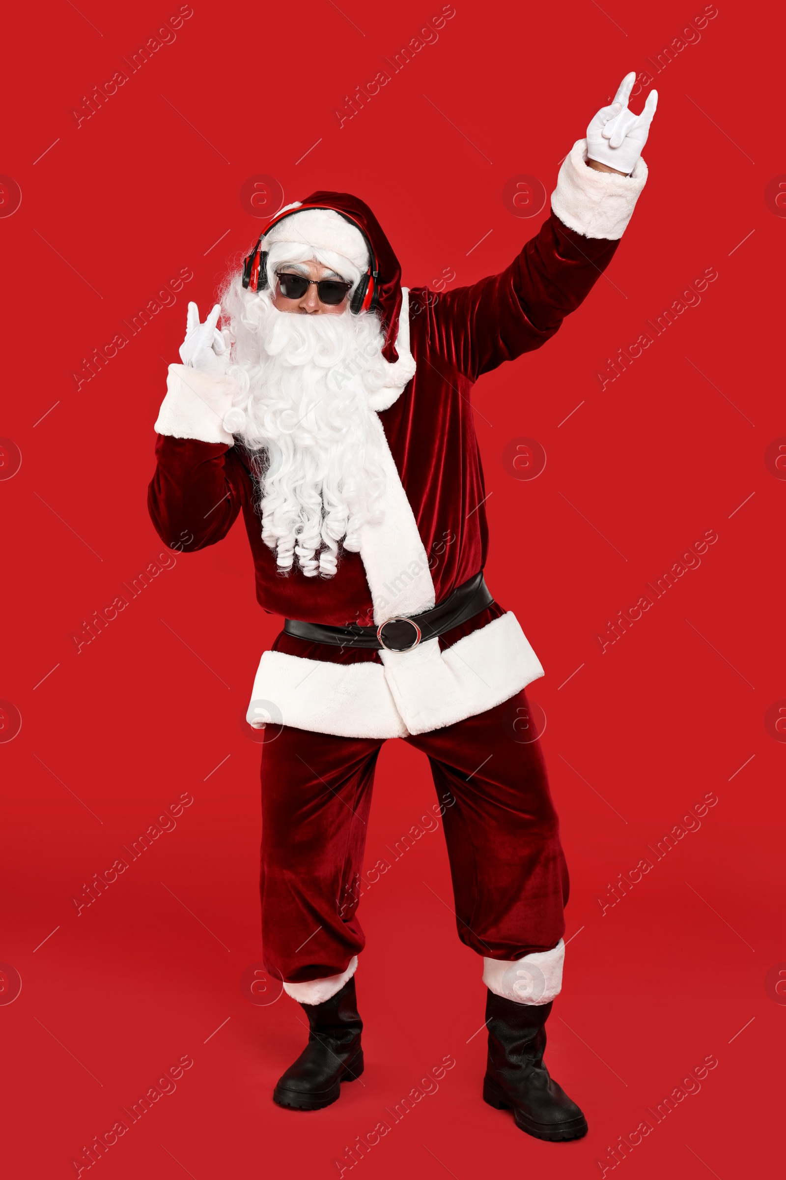 Photo of Santa Claus with headphones listening to Christmas music on red background