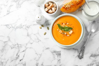 Delicious pumpkin soup in bowl on marble table, flat lay. Space for text